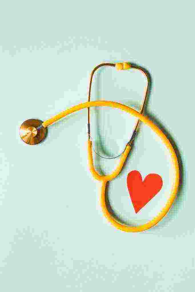Medical stethoscope with red paper heart on white surface