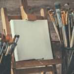 Artistic equipment: empty artist canvas on easel and paint brushes in a artist studio. Retro toned photo.