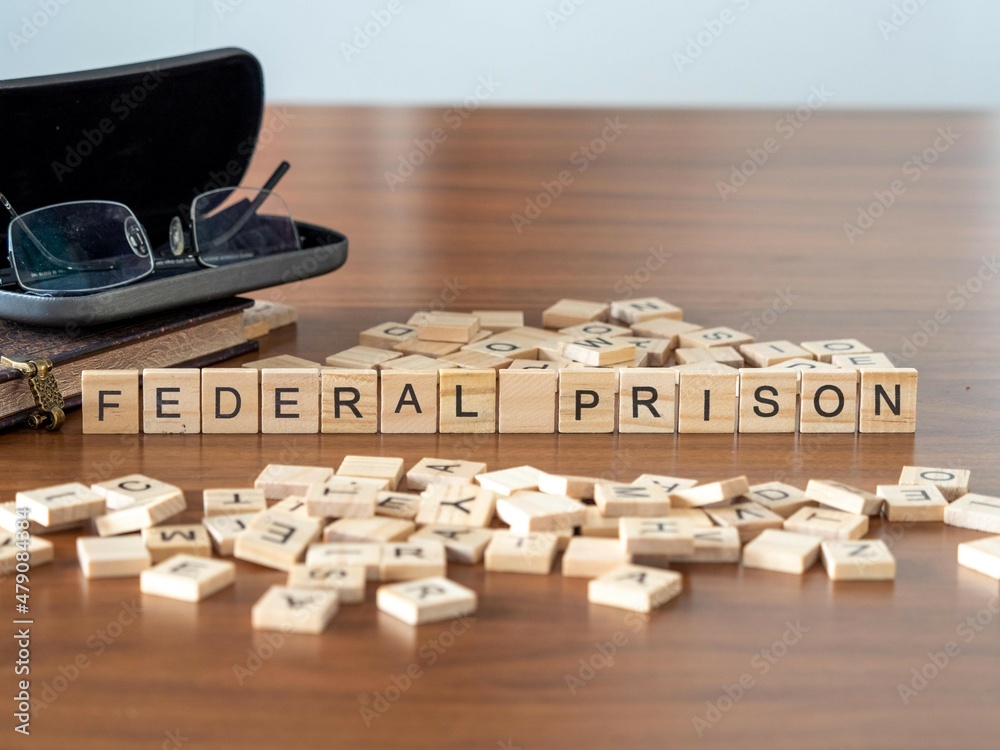 federal prison concept represented by wooden letter tiles on a wooden table with glasses and a book