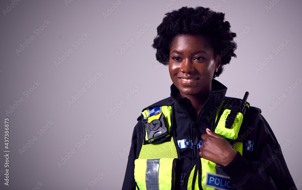 Studio Portrait Of Smiling Young Female Police Officer Against Plain Background