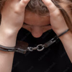 A young girl handcuffed on a gray background, close-up. Juvenile delinquent in a black T-shirt, criminal liability of minors.