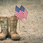 Old military combat boots with dog tags and two small American flags. Rocky gravel background with copy space. Memorial Day or Veterans day concept.