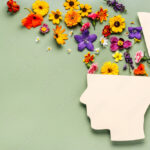 World mental health day concept. Paper human head symbol and flowers on blue background